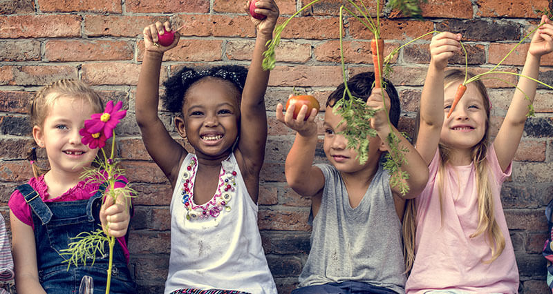 inspiring-young-minds-apply four children leaning against a wall holing flowers and carrots